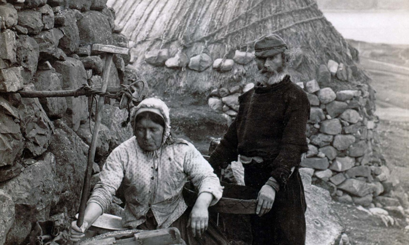A woman and man working outside a stone cottage on the island of St. Kilda in the 1880s.